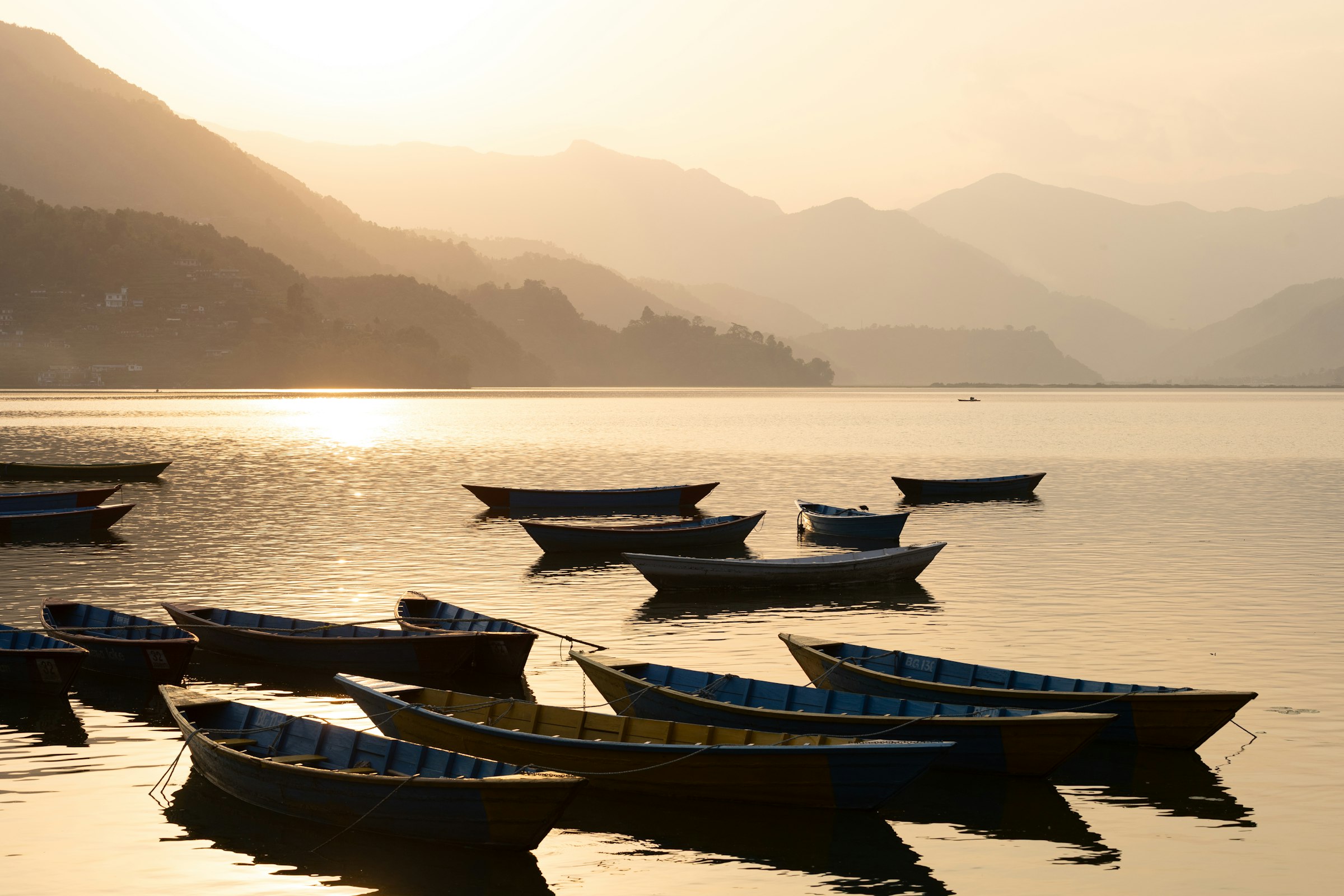 Wooden boats moored on Phewa Lake at sunset, with the hills above Pokhara behind